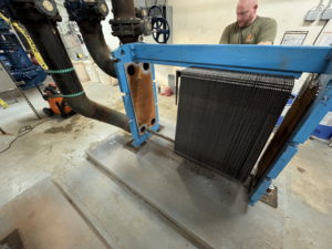 A technician servicing a commercial plate heat exchanger, exposing the internal components for APEX HVAC Solutions LLC in Frederick, MD.