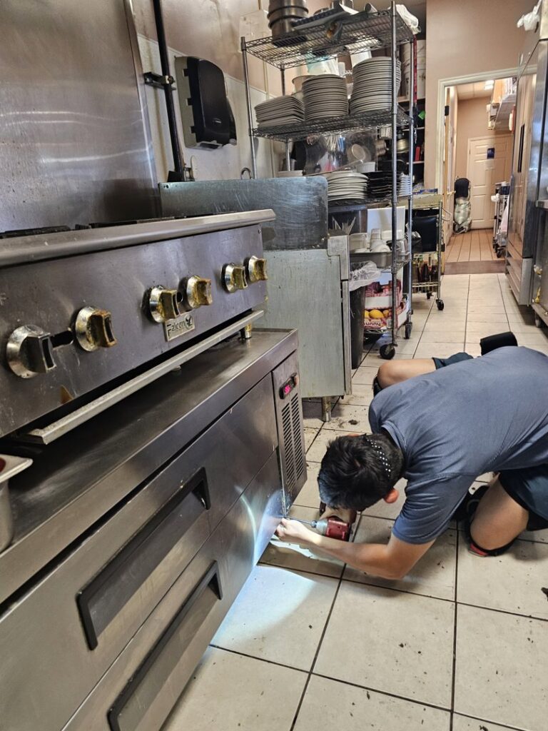 A technician servicing a commercial refrigeration unit in a kitchen for Henry Refrigeration & Hvac Utah in Ogden, UT.