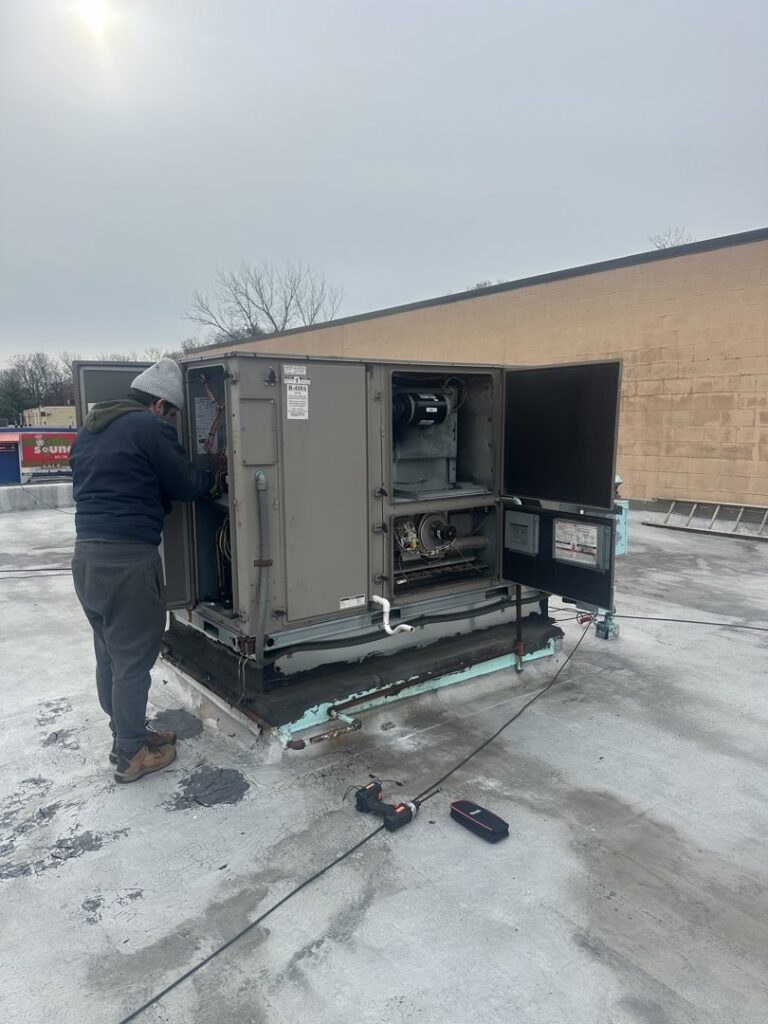 A technician from Indoor Expert Heating & Cooling servicing a large commercial rooftop HVAC unit in Paterson, NJ.