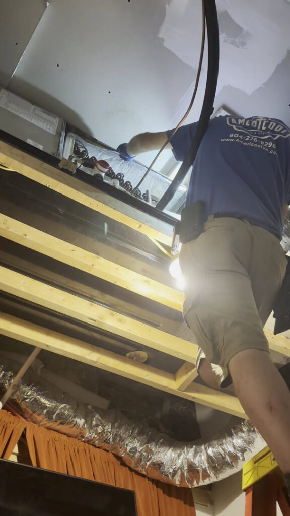 An Americool Heating & Cooling technician servicing ductwork or an indoor unit in a ceiling in Richmond, VA.