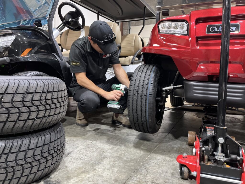 A Cart Electric technician servicing the front wheel and electrical components of a red electric golf cart in Nashville, TN.