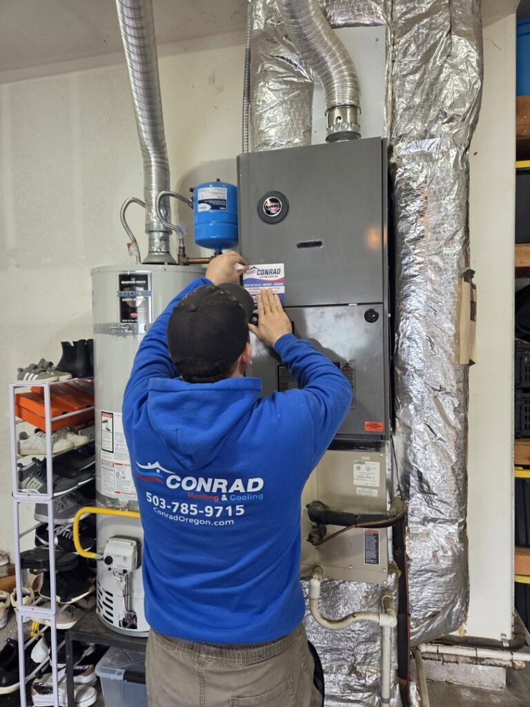 A Conrad Heating and Cooling technician servicing a furnace or air handler in Beaverton, OR.