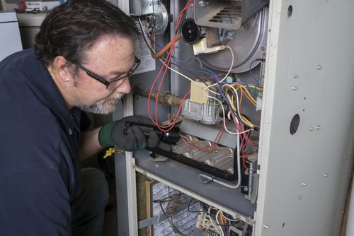 A technician servicing a furnace with the panel open for Daniels HVAC Philadelphia LLC in Philadelphia, PA.