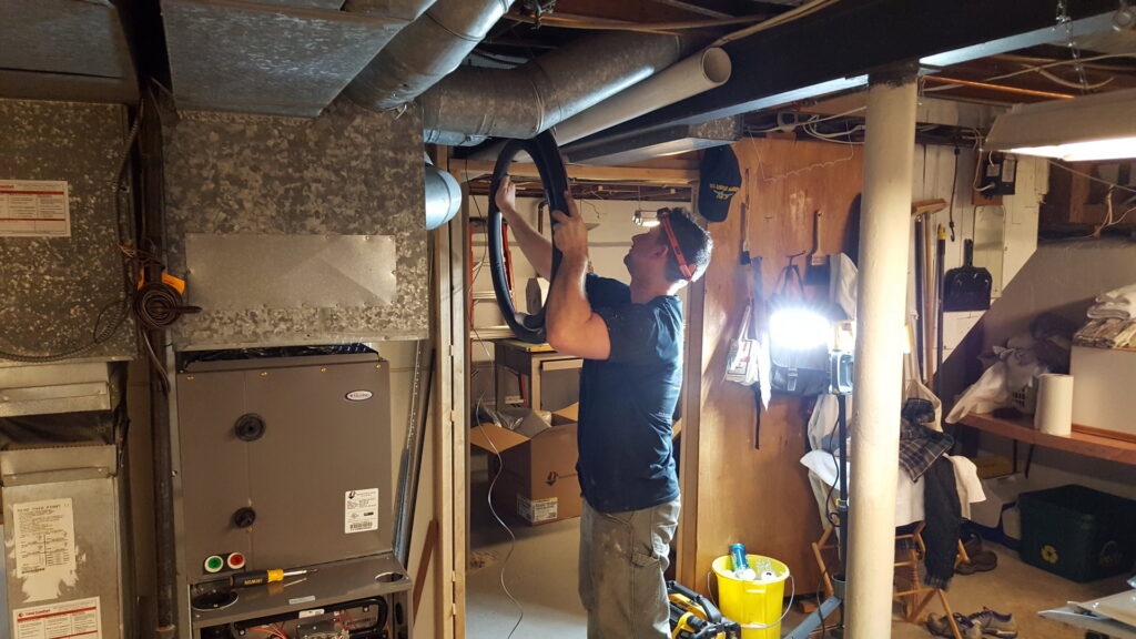 A technician from Total Comfort Heat and Air Conditioning, Inc. servicing an indoor furnace in Rochester, NY.