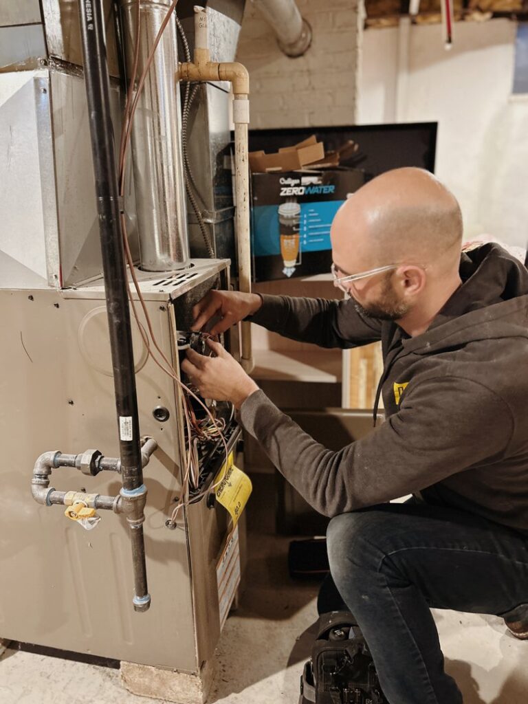 A skilled technician from Davis Heating, Air Conditioning & Home servicing an open furnace unit in a residential basement in Overland Park, KS.