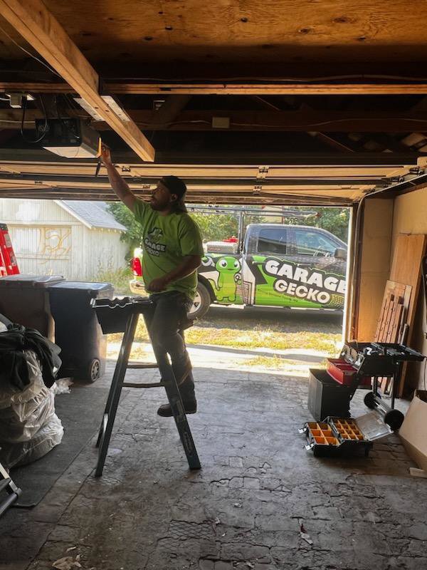 A Garage Gecko technician servicing a garage door opener mechanism from a step stool in Spokane, WA.