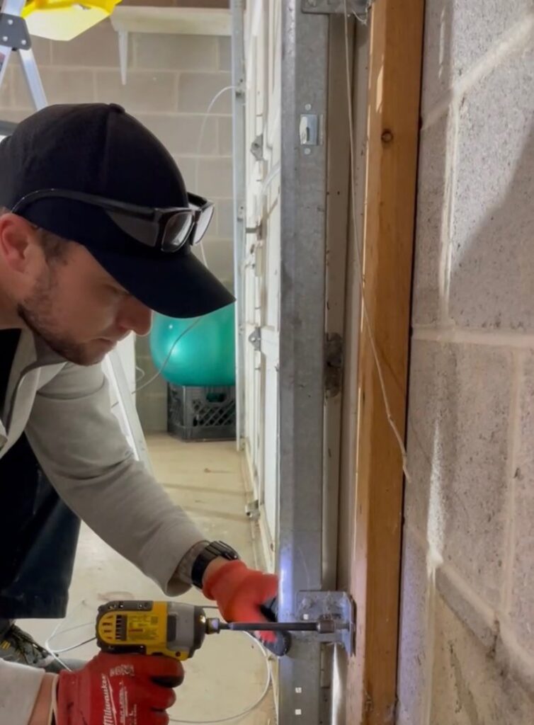 A technician servicing a garage door roller and hinge with a power drill for Align Garage Door in Ringgold, GA.