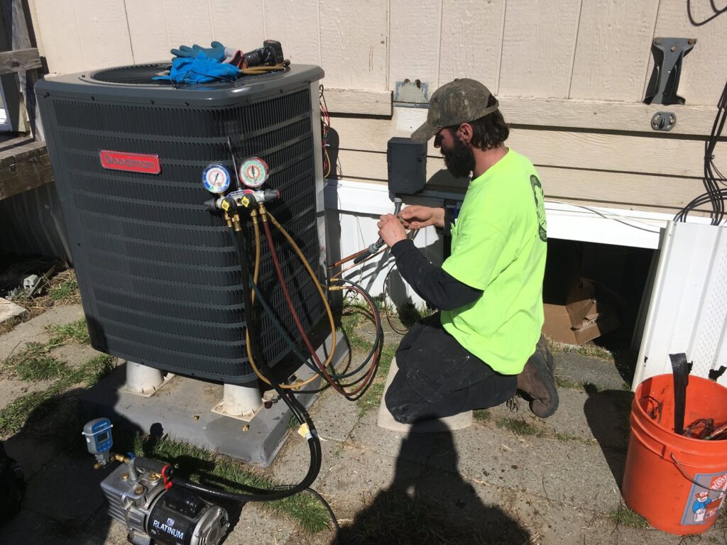 An R&R Heating & Air Conditioning technician servicing an outdoor Goodman AC unit with gauges in Spokane, WA.