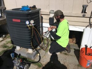 An R&R Heating & Air Conditioning technician servicing an outdoor Goodman AC unit with gauges in Spokane, WA.