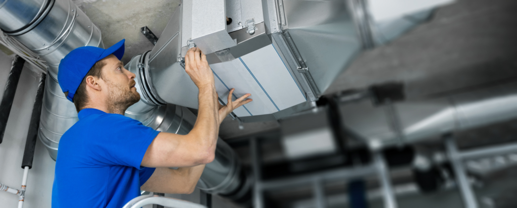 A technician in a blue uniform servicing HVAC ductwork and changing a filter for Purair Hawaii in Honolulu, HI.