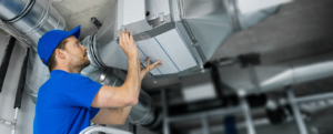 A technician in a blue uniform servicing HVAC ductwork and changing a filter for Purair Hawaii in Honolulu, HI.