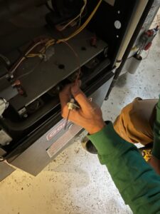 A TAS Mechanical Services technician servicing an HVAC furnace unit with a tool, performing maintenance in Kearney, MO.