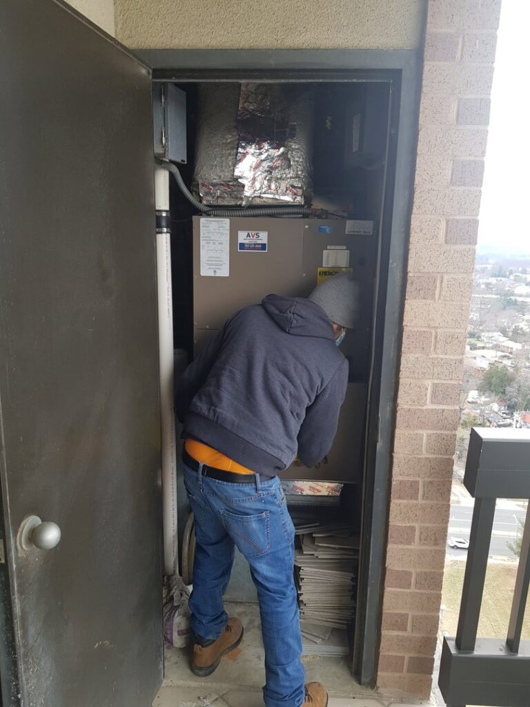 A technician from AVS Heating and Air Conditioning servicing an indoor HVAC unit in Alexandria, VA, demonstrating professional service.