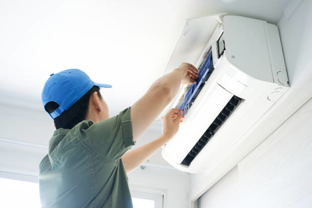A technician in a blue cap servicing an indoor split AC unit, a common service provided by Desert Peaks in Phoenix, AZ.