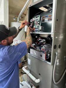 A technician from ACI Northwest Heating, Cooling & Electrical servicing an indoor furnace or air handler unit in Dalton Gardens, ID.