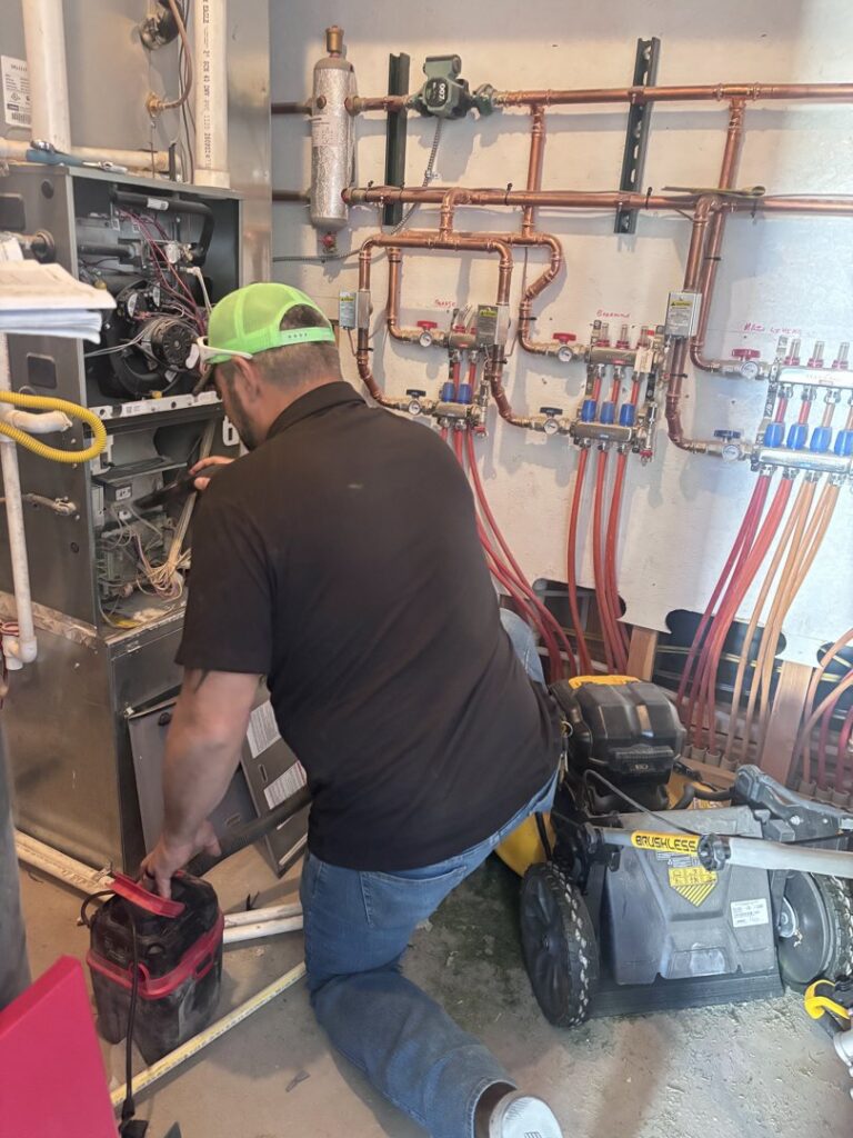 A technician from Lee's Heating & Cooling servicing an indoor furnace or boiler system in Pueblo, CO.
