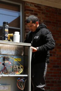 A Green Dot Heating & Air technician servicing an indoor HVAC unit with exposed wiring in Wilmington, NC.