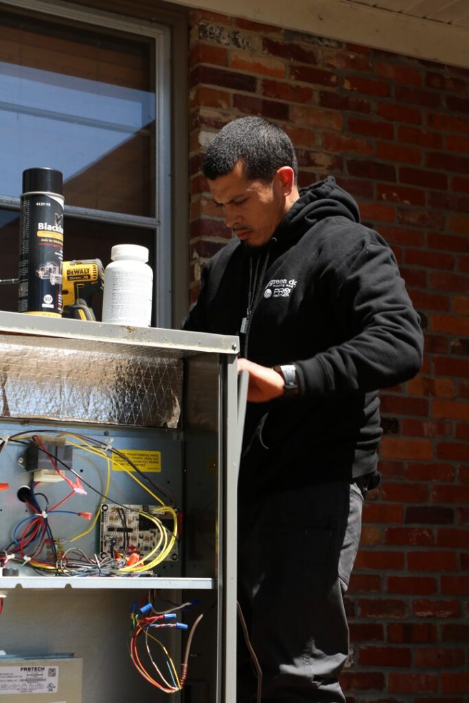 A Green Dot Heating & Air technician servicing an indoor HVAC unit with exposed wiring in Wilmington, NC.