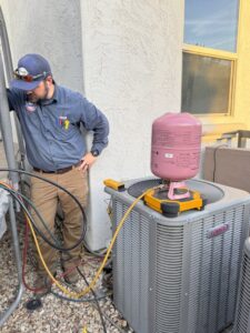 A technician from Rusty's Air Conditioning And Heating servicing a Lennox AC unit with gauges and refrigerant in Mesa, AZ.