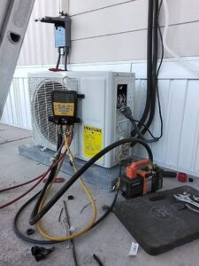 A technician servicing an outdoor mini-split HVAC unit with gauges and a vacuum pump for Heating & Air Paramedics - Tucson in Tucson, AZ.
