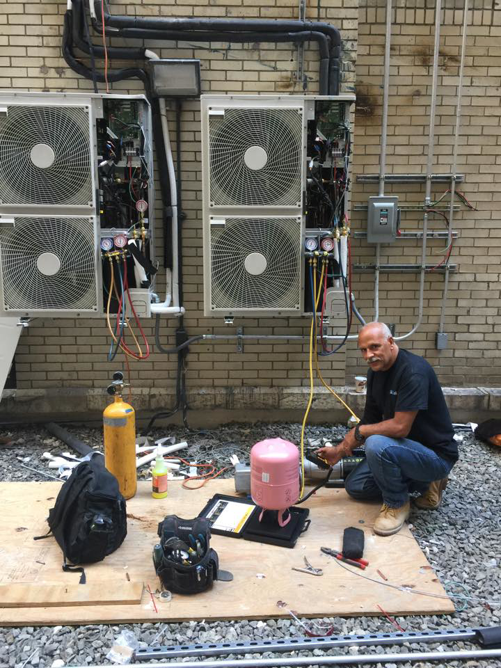 A technician servicing multiple outdoor HVAC units with refrigerant gauges and tanks at aghapy 1 in Jersey City, NJ