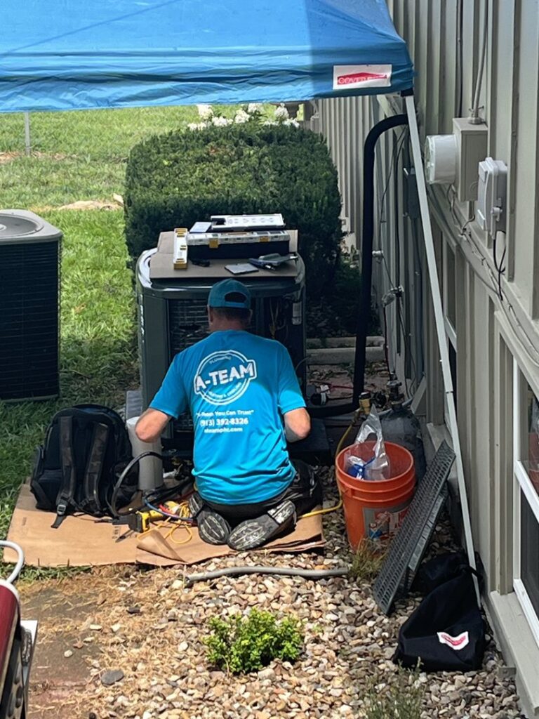 An A-Team PHC technician performing maintenance on an outdoor AC unit in Olathe, KS.