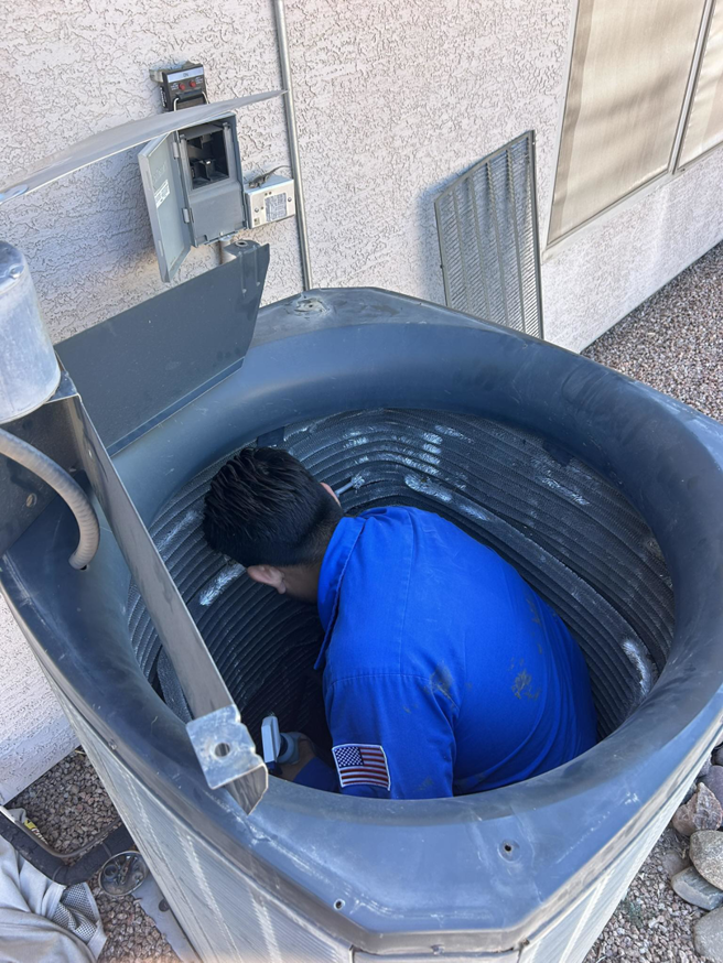 A technician servicing an outdoor AC unit, cleaning coils for A/C Valley, LLC in Tempe, AZ.