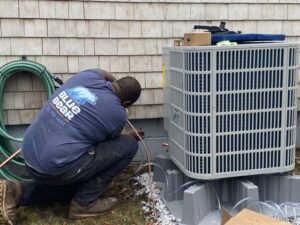 A Blue Bear Plumbing, Heating, & Air technician servicing an outdoor air conditioning unit in Norwell, MA.
