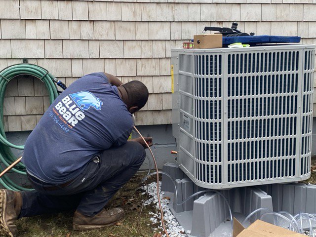 A Blue Bear Plumbing, Heating, & Air technician servicing an outdoor air conditioning unit in Norwell, MA.