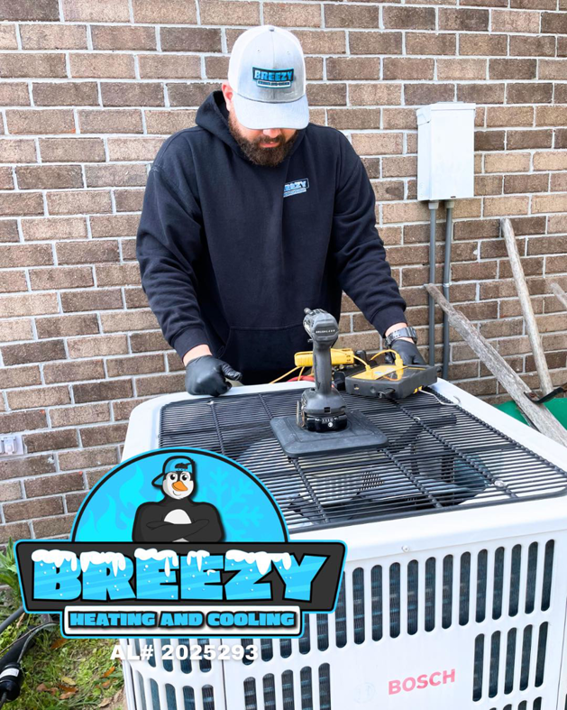A Breezy Heating and Cooling technician servicing an outdoor AC unit in Mobile, AL.