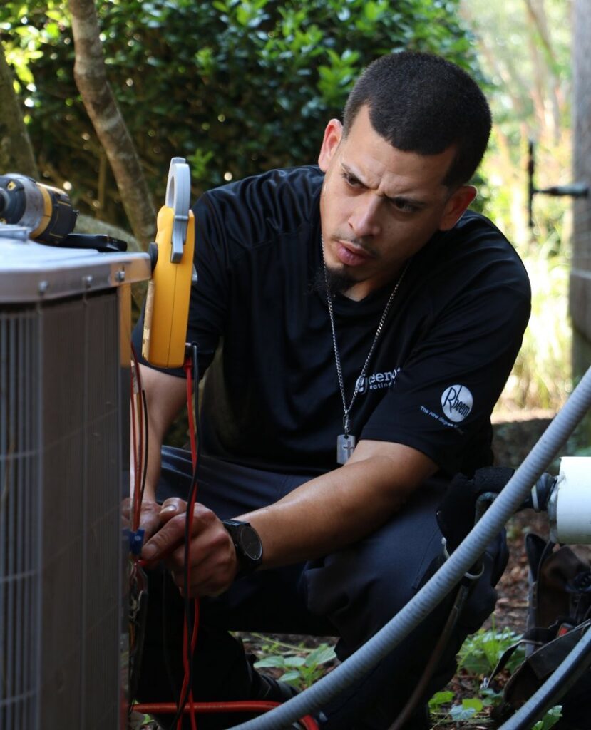 A Green Dot Heating & Air technician servicing an outdoor AC unit with a clamp meter in Wilmington, NC.