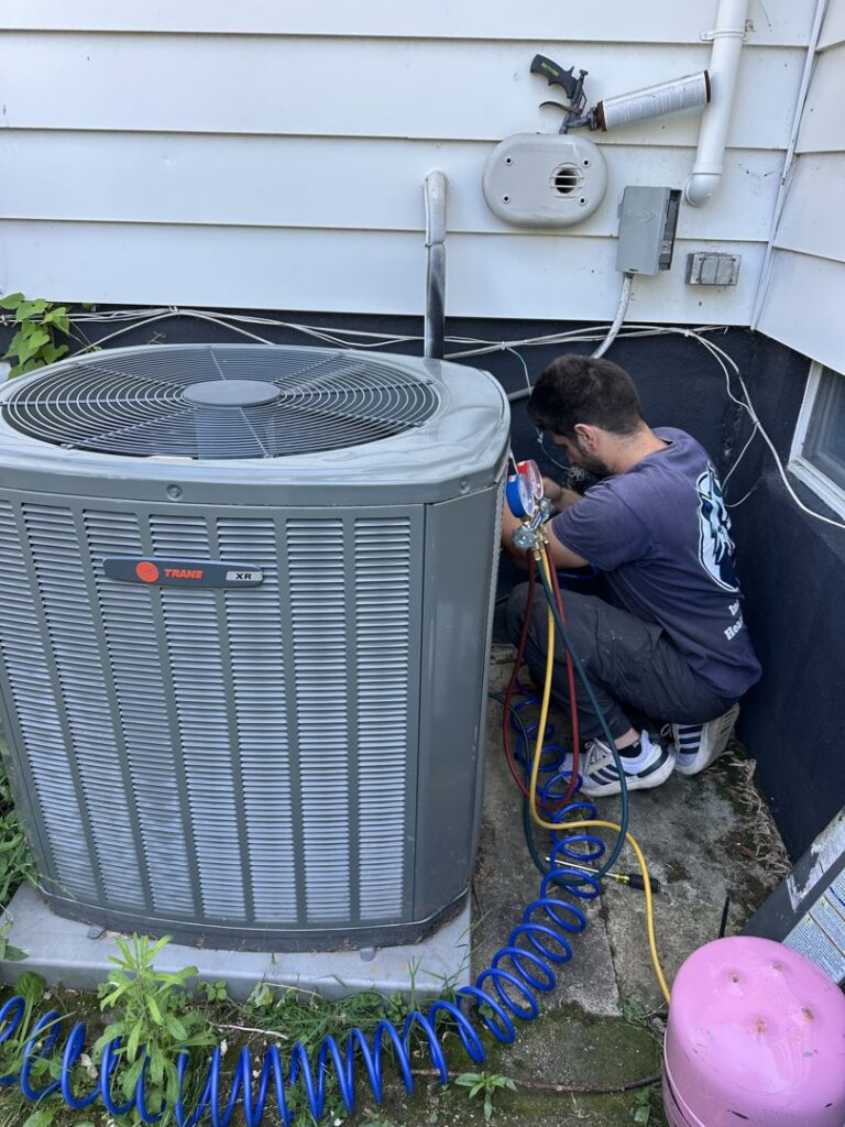 A technician from Indoor Expert Heating & Cooling servicing an outdoor Trane XR air conditioning unit with gauges in Paterson, NJ.