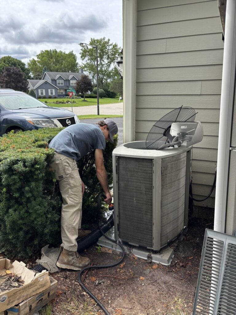 A technician from Nordic Air Heating & Cooling servicing an outdoor air conditioning unit in West Allis, WI.