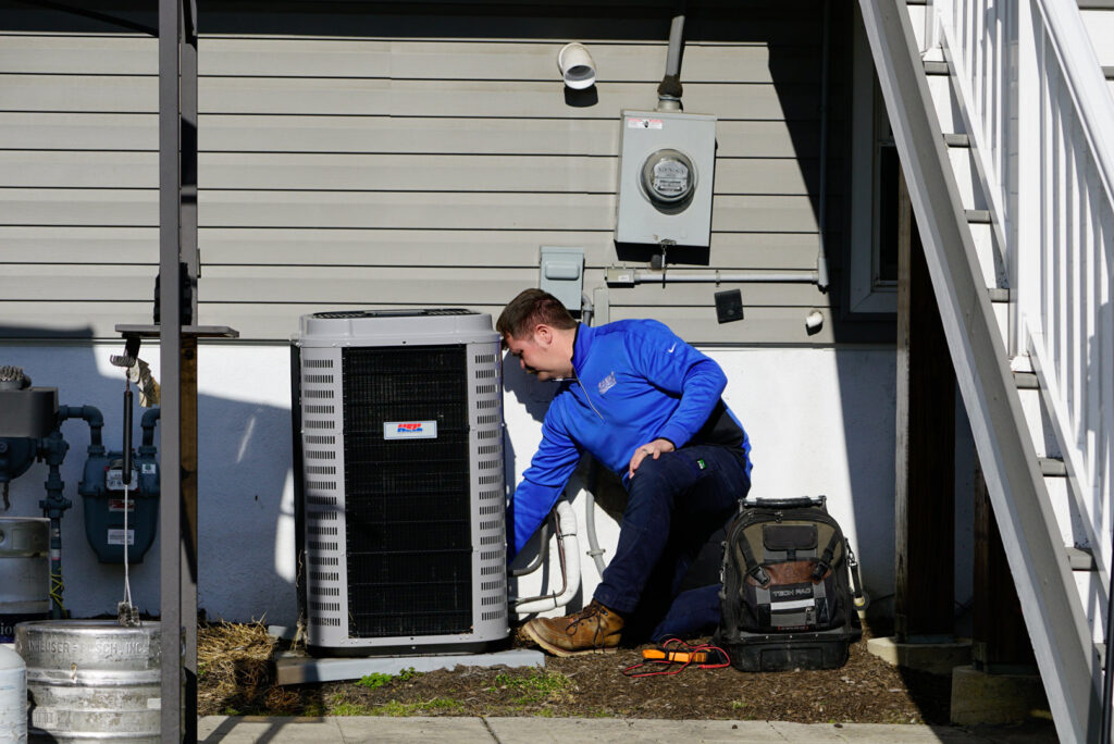A SANKS Mechanical technician kneeling to service an outdoor air conditioning unit at a residential property in Philadelphia, PA.