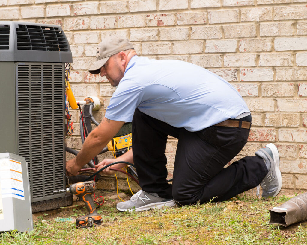 A technician servicing an outdoor AC unit for Thomas Service Company in Huntsville, AL