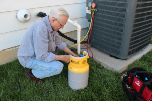 A technician servicing an outdoor air conditioning unit with gauges and a refrigerant tank for West Wichita Heating & Air Conditioning in Wichita, KS.