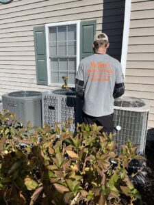 A technician from McTeer's Heating & Cooling in Salisbury, MD, servicing outdoor air conditioning units at a residential property.