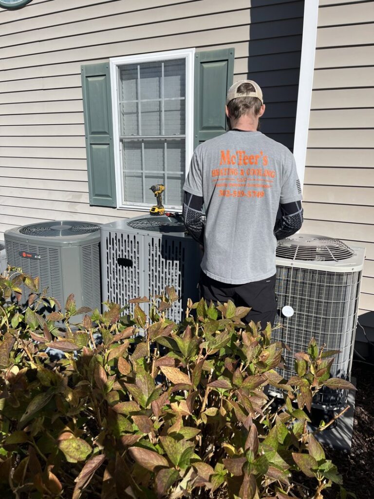 A technician from McTeer's Heating & Cooling in Salisbury, MD, servicing outdoor air conditioning units at a residential property.