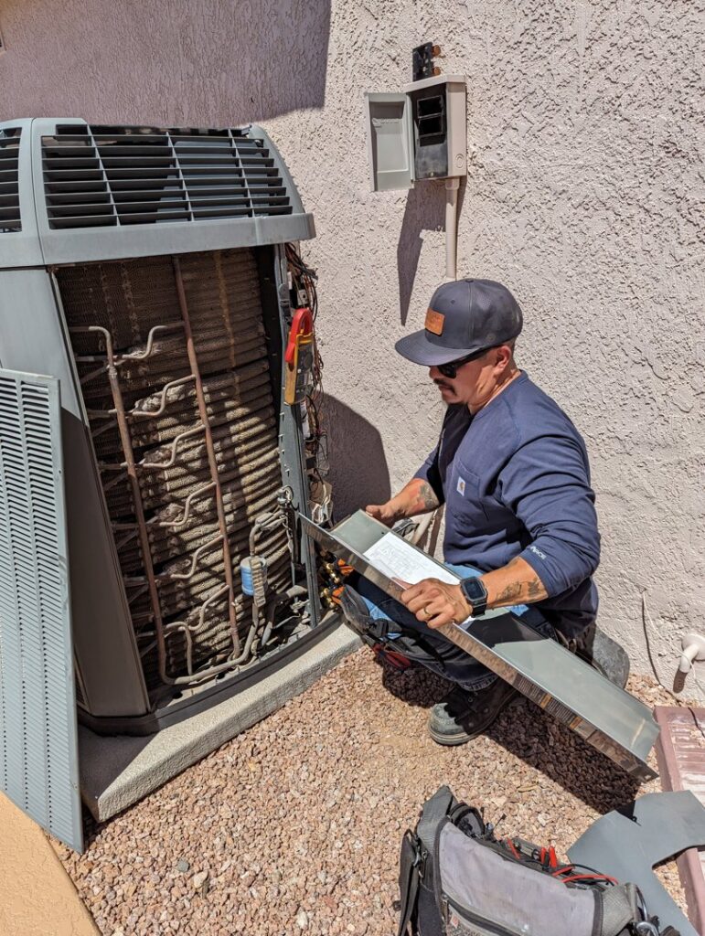 A technician servicing an outdoor HVAC condenser unit with exposed coils for maintenance by Blue Collar Mechanical LLC in Indianapolis, IN.