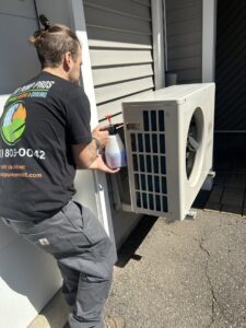 A Heat Pump Pros technician servicing an outdoor mini-split heat pump unit with a spray in Hartford, CT.