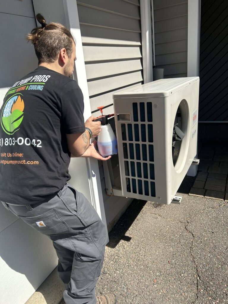 A Heat Pump Pros technician servicing an outdoor mini-split heat pump unit with a spray in Hartford, CT.