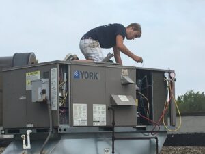 A technician performing service on a commercial rooftop HVAC unit for Adams Heating and Cooling in Schenectady, NY
