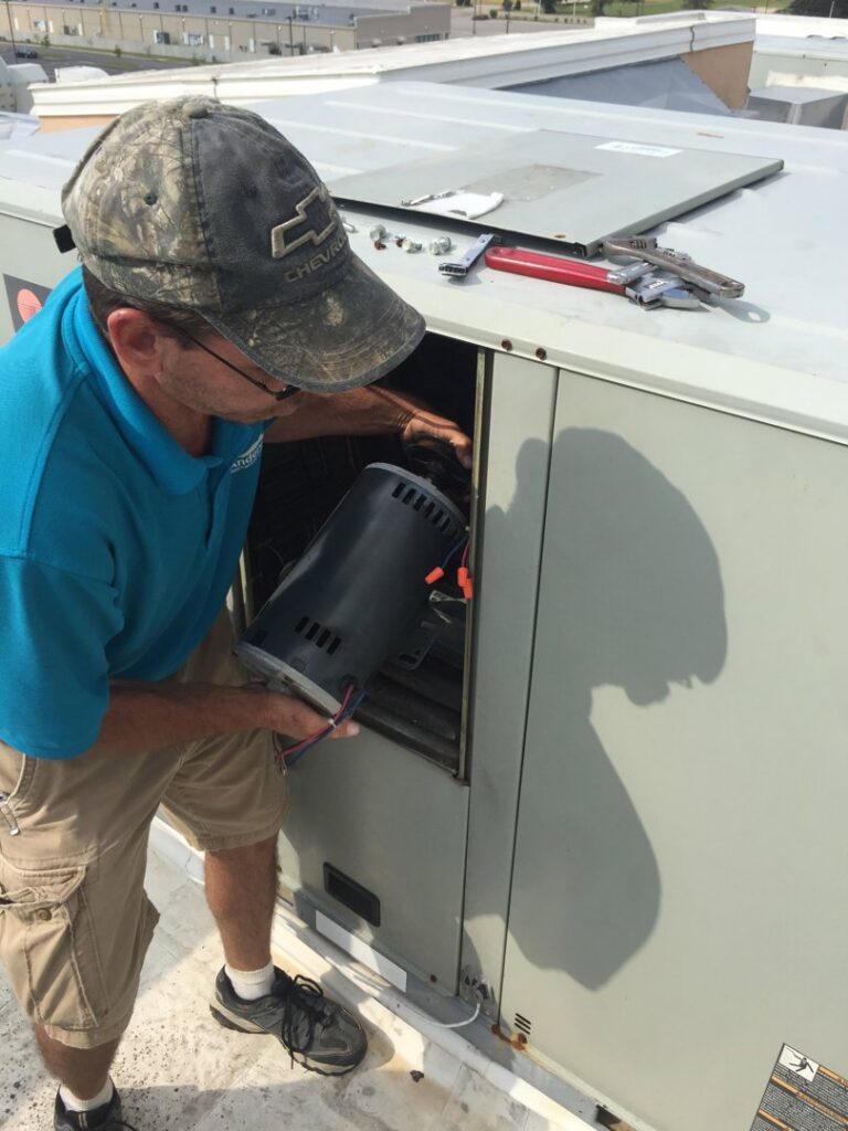 A technician servicing a commercial rooftop HVAC unit, holding a component, for Anderson Mechanical Inc. in Pascagoula, MS