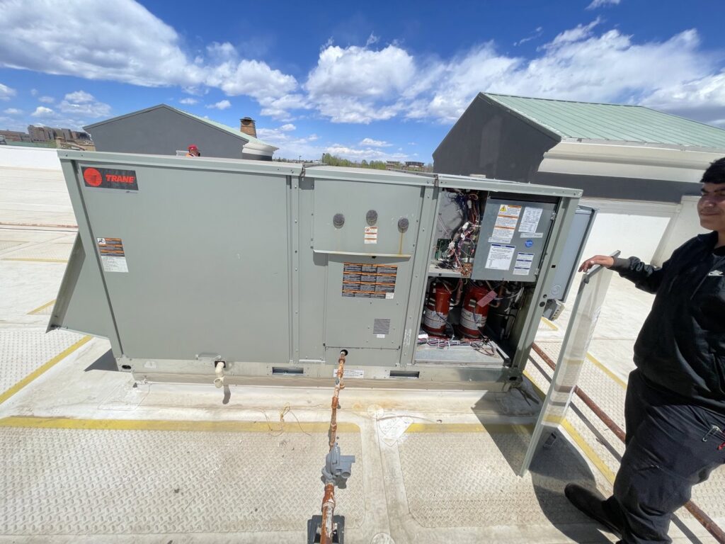 A technician performing service and maintenance on a commercial rooftop HVAC unit for CHAMPS Heating&Air in Denver, CO
