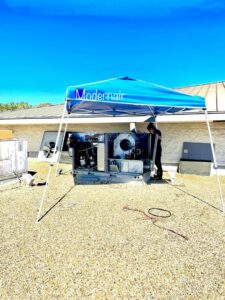 A Modern Air Services technician servicing a large rooftop HVAC unit under a canopy in Fort Worth, TX.