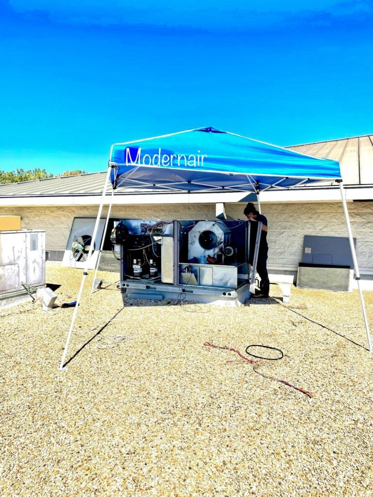 A Modern Air Services technician servicing a large rooftop HVAC unit under a canopy in Fort Worth, TX.