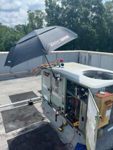 A technician servicing a rooftop HVAC unit with tools and an umbrella for shade by TAG Heat N Air in North Little Rock, AR.