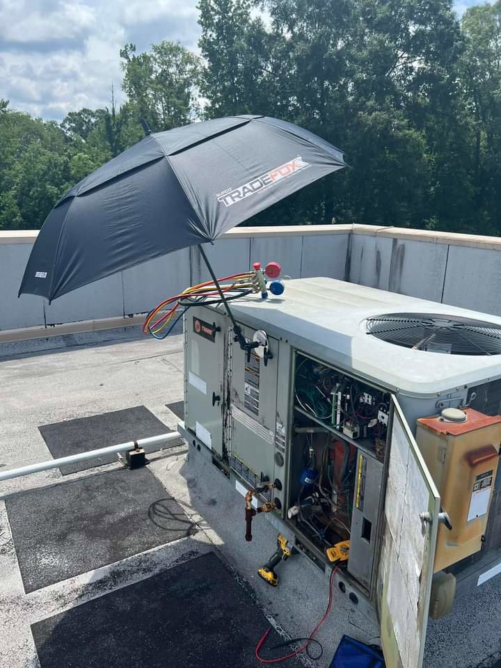 A technician servicing a rooftop HVAC unit with tools and an umbrella for shade by TAG Heat N Air in North Little Rock, AR.