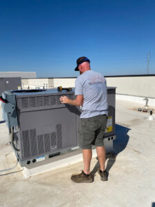 A technician from TK Heating and Air, PLLC servicing a commercial rooftop HVAC unit in Queen Creek, AZ