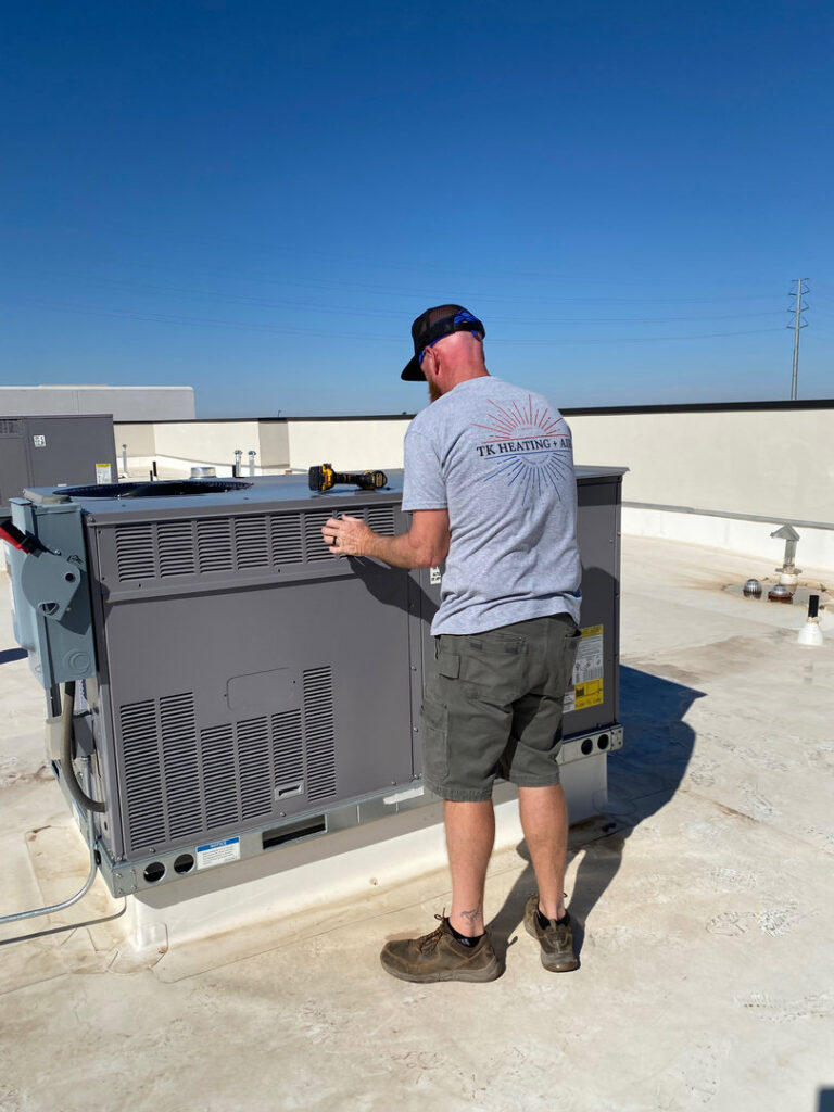 A technician from TK Heating and Air, PLLC servicing a commercial rooftop HVAC unit in Queen Creek, AZ